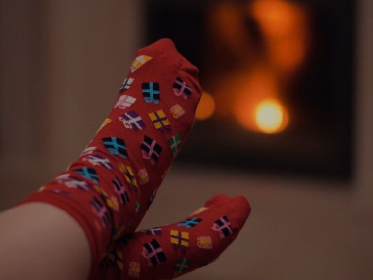 Osoba nosi čarape sa poklonima i greje se o kamin